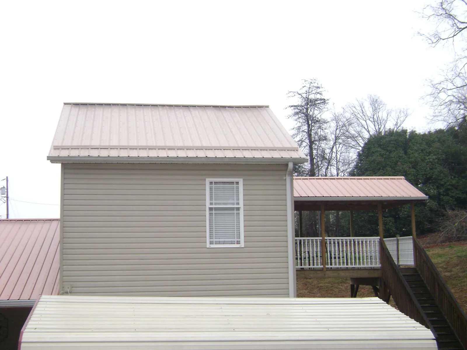 Tan metal roofs on a two story addition and attached porch, from a Roof Replacement job in Hamburg